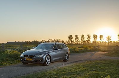A bmw is parked on the side of a road in a field at sunset.