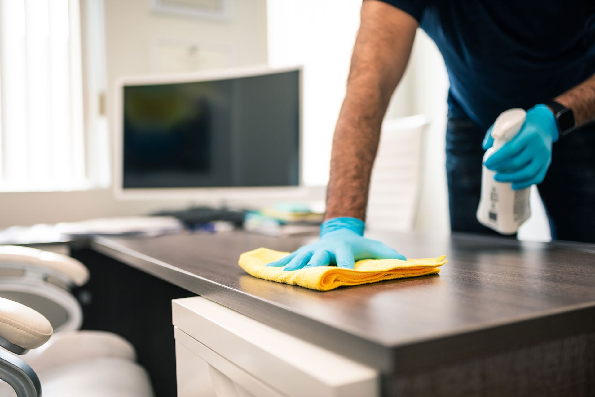 A man is cleaning a desk with a cloth and spray bottle