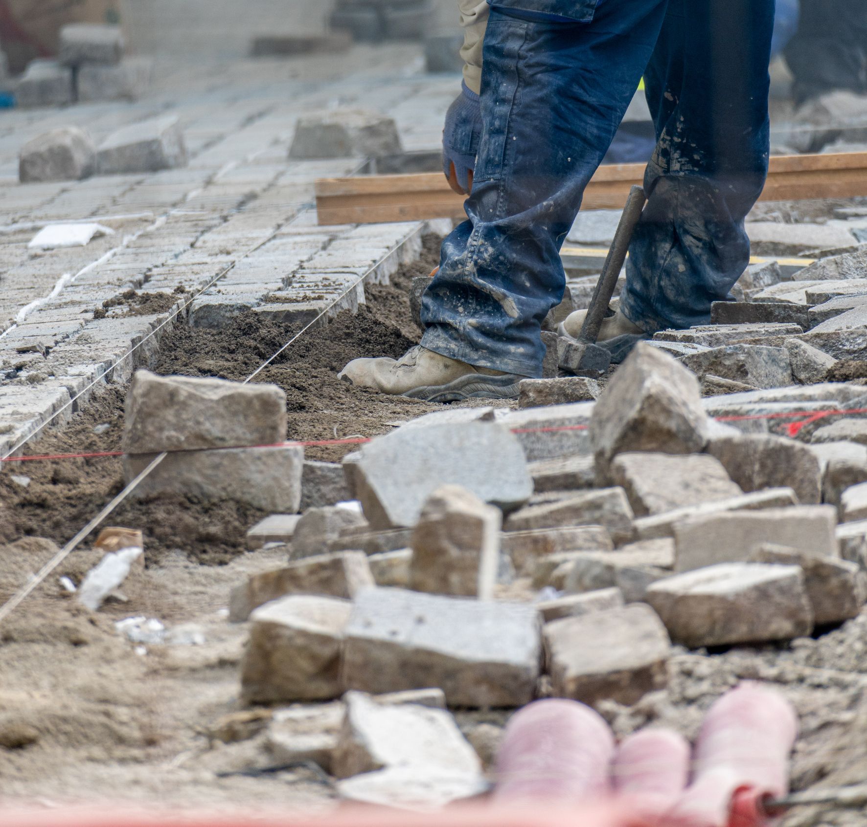 A man is laying bricks on a sidewalk with a shovel.