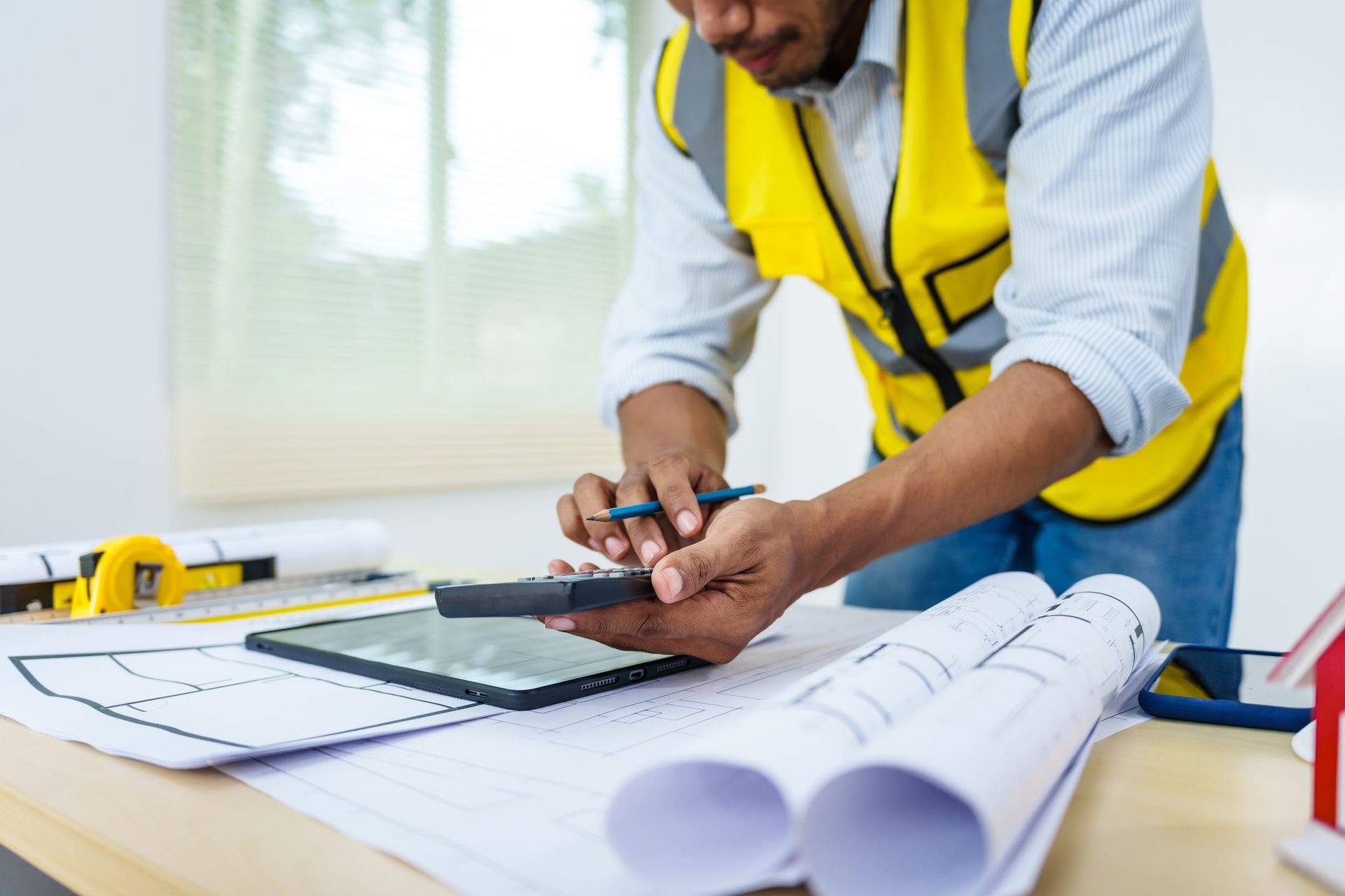 A man in a yellow vest is using a tablet and a calculator.