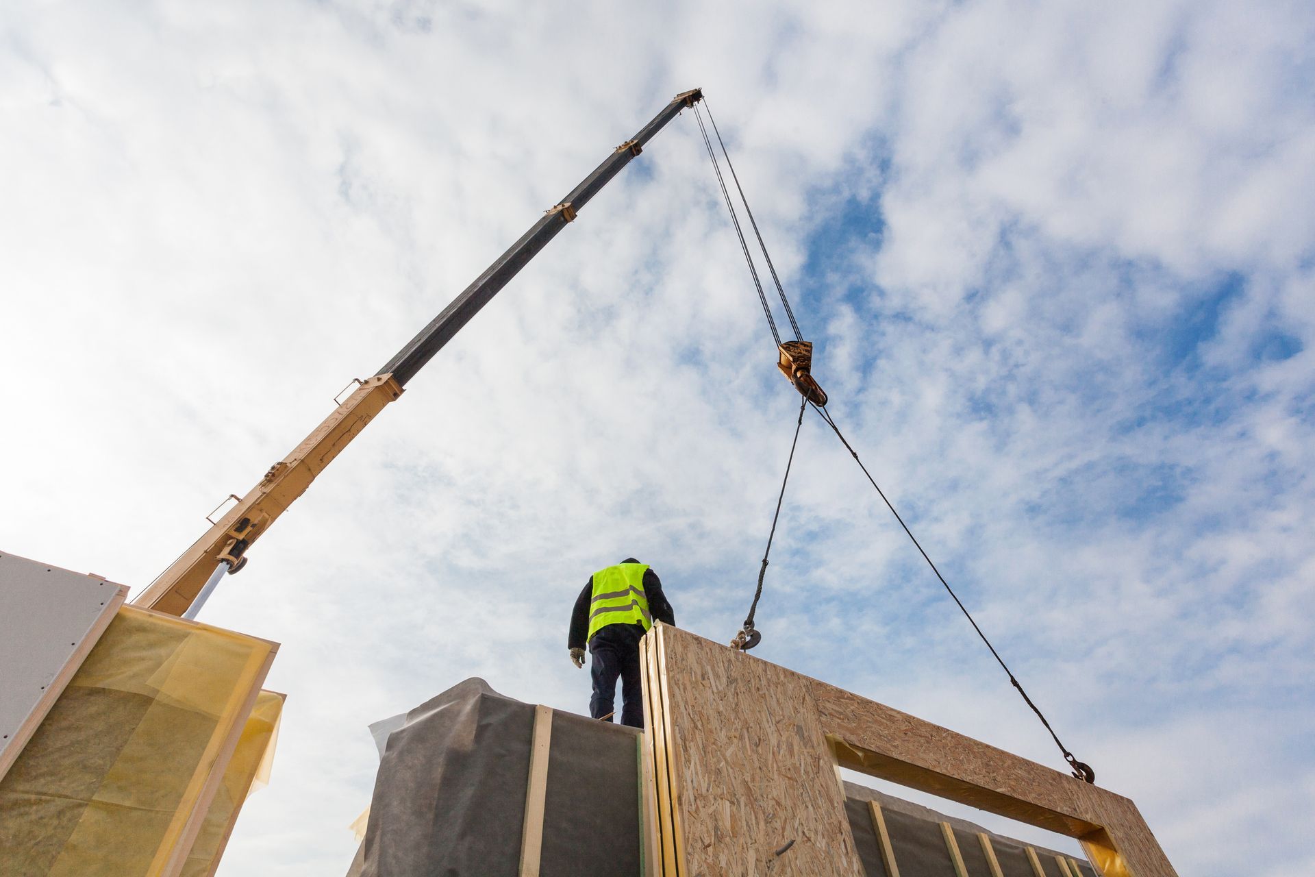 A man is standing on top of a building being lifted by a crane.