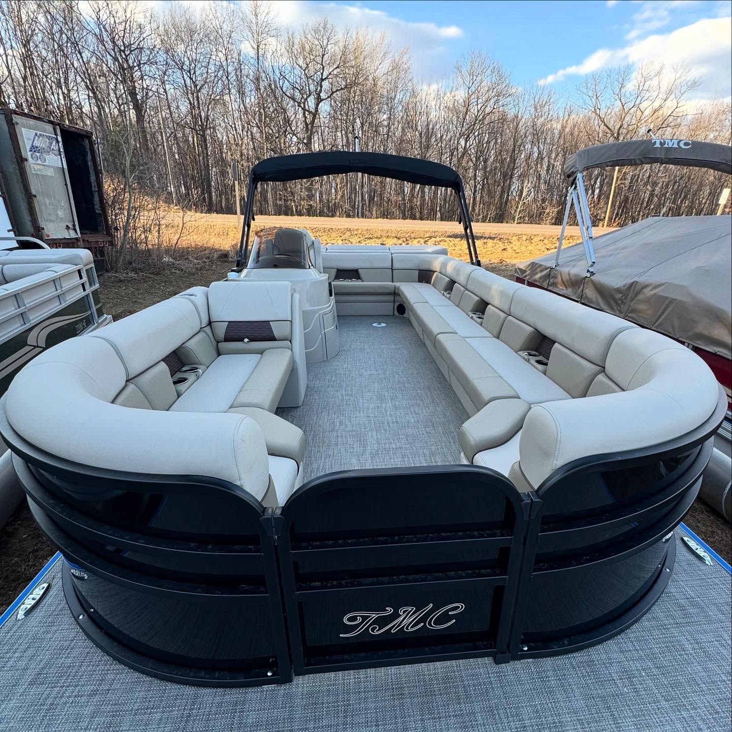 Black pontoon boat with beige seating and canopy. Outdoors.