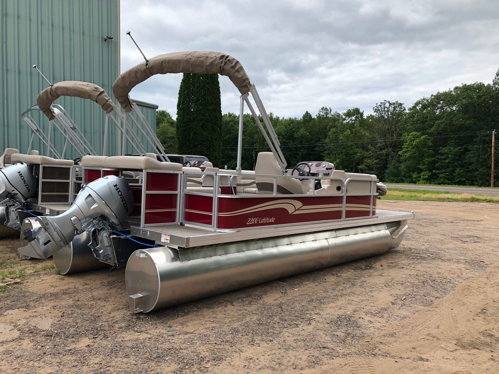 Black and beige pontoon boat on land, with seating and a canopy.
