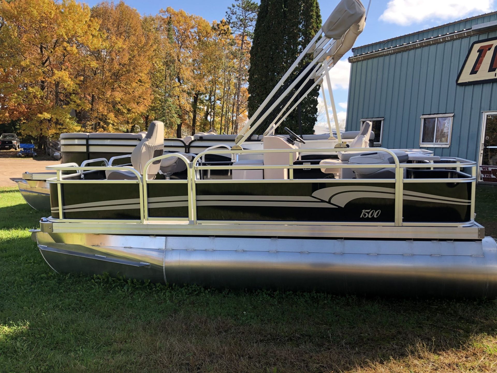 Black and silver pontoon boat on green grass, with a building and fall trees in the background.