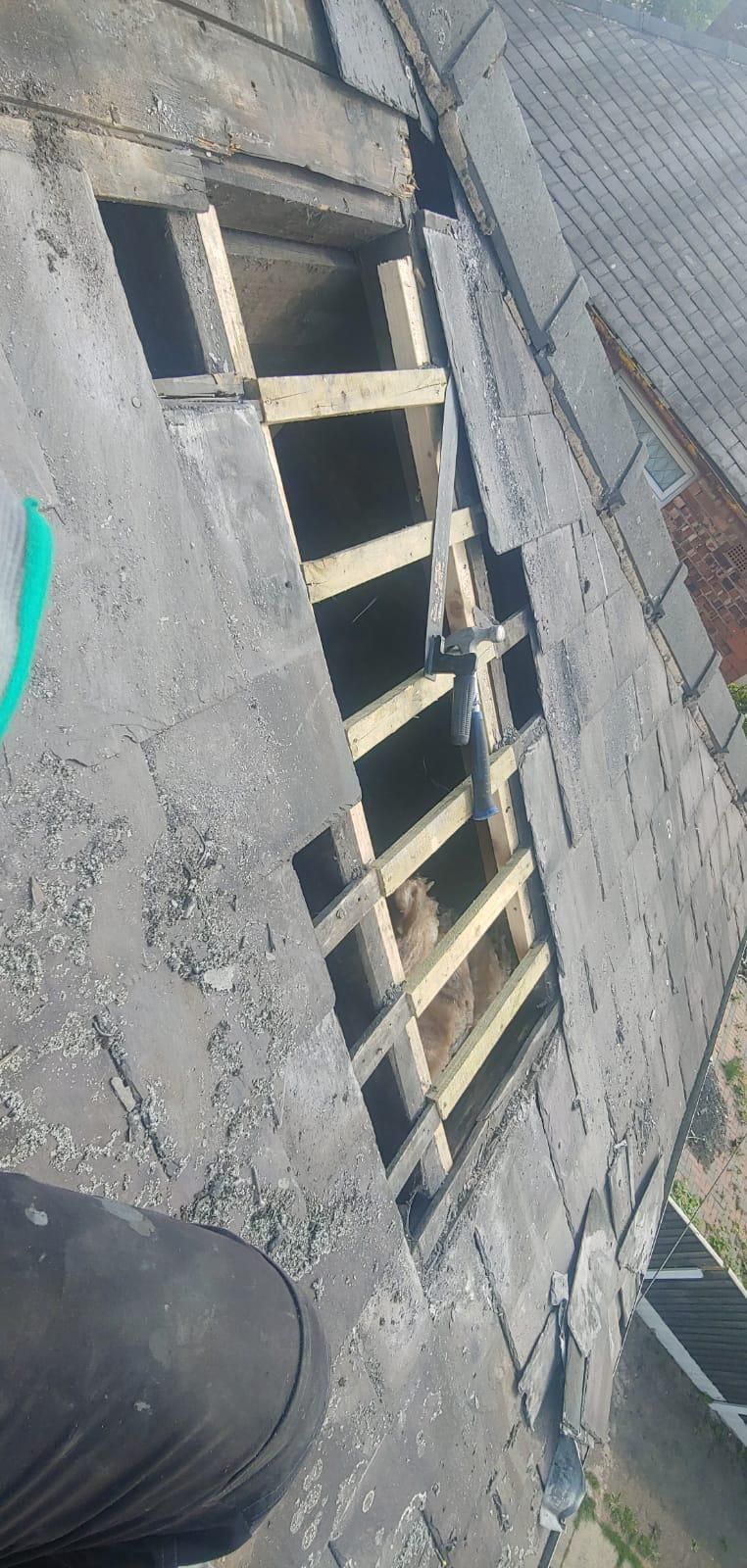 A damaged roof with missing tiles exposing wooden supports. The angle suggests a person is standing on the roof.