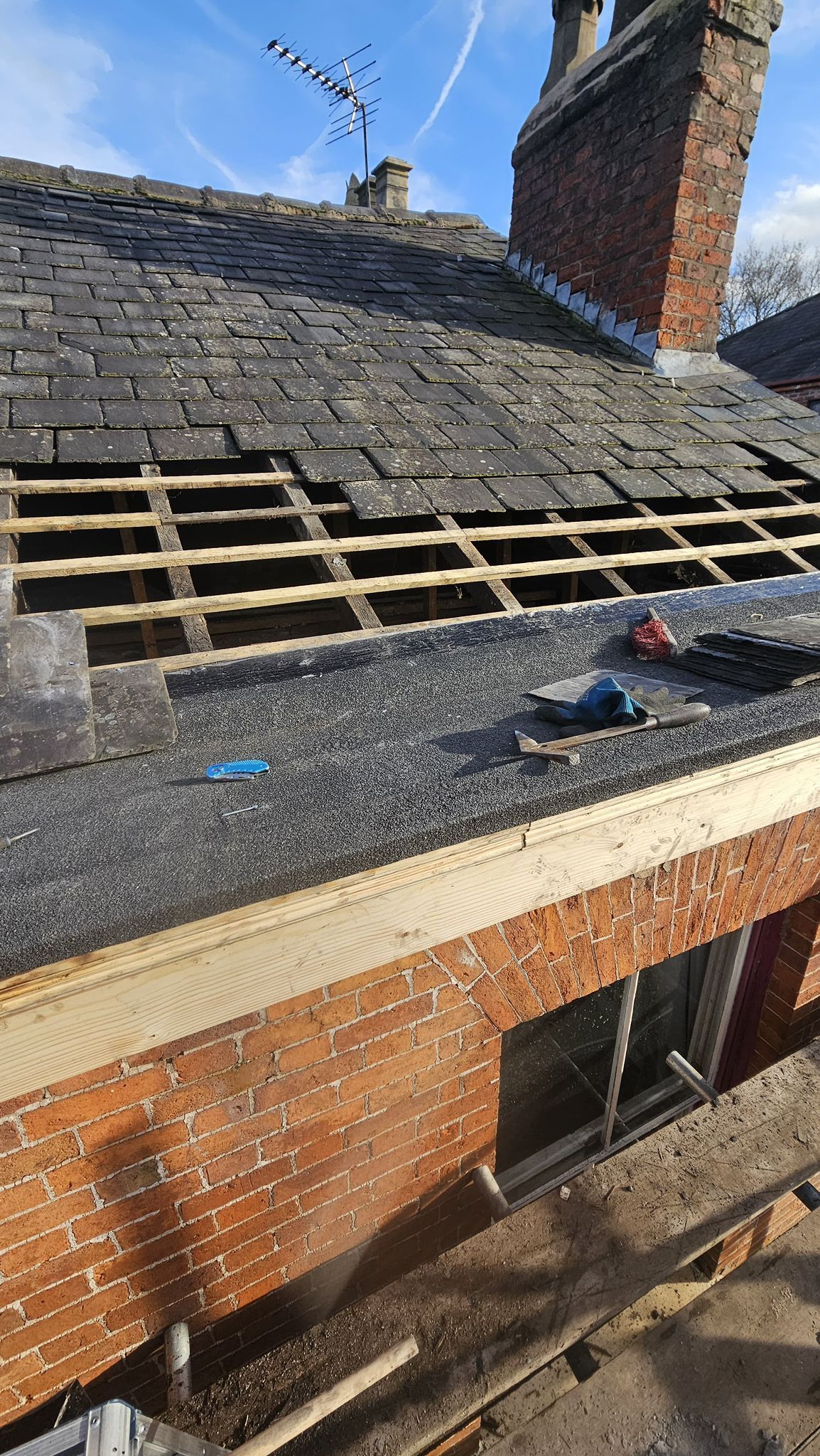 Roof partially uncovered during renovation, showing wooden frame, chimney, and brickwork.