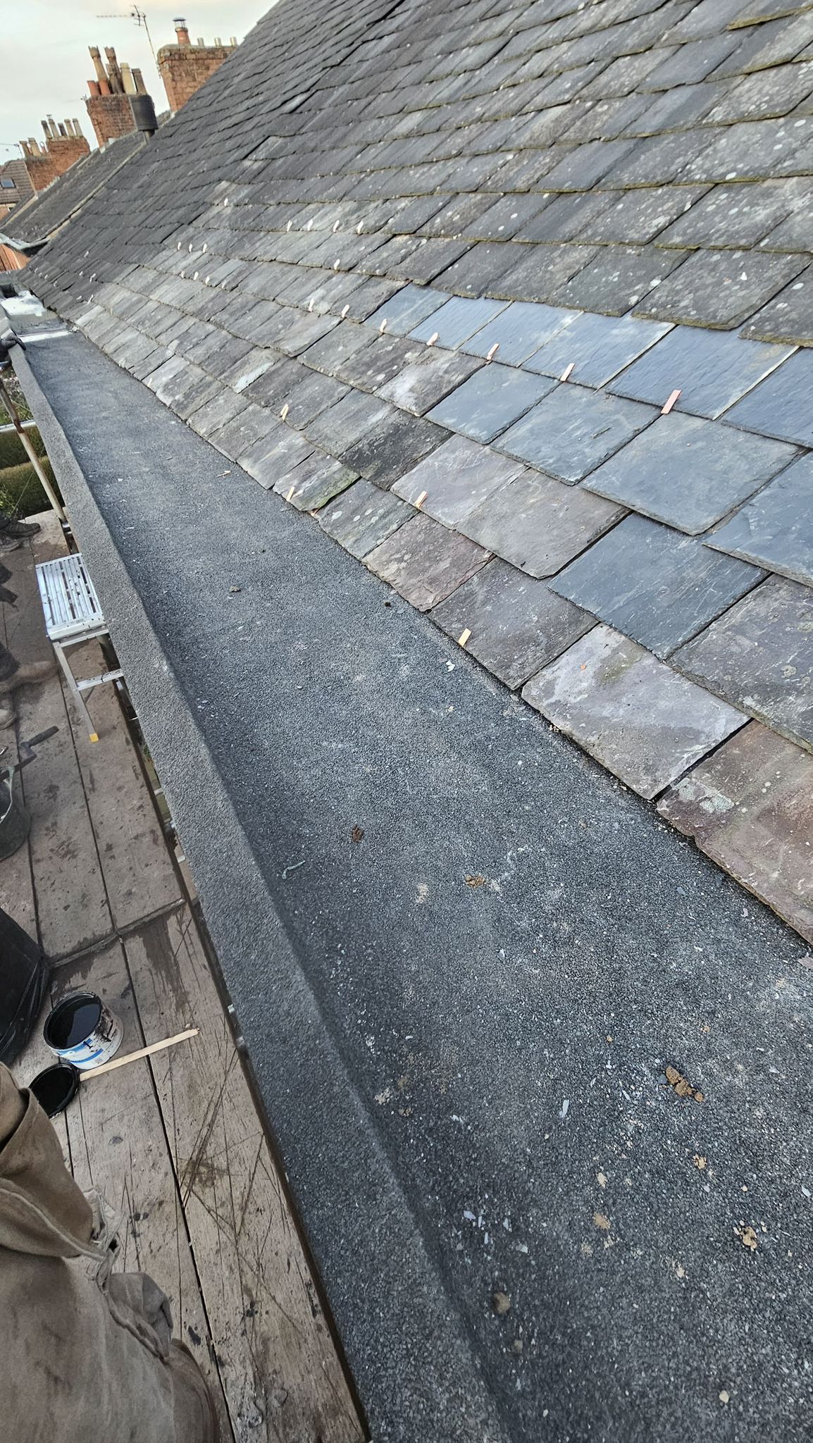 Slate roof with weathered, dark gray gutter and rooftop tiles.