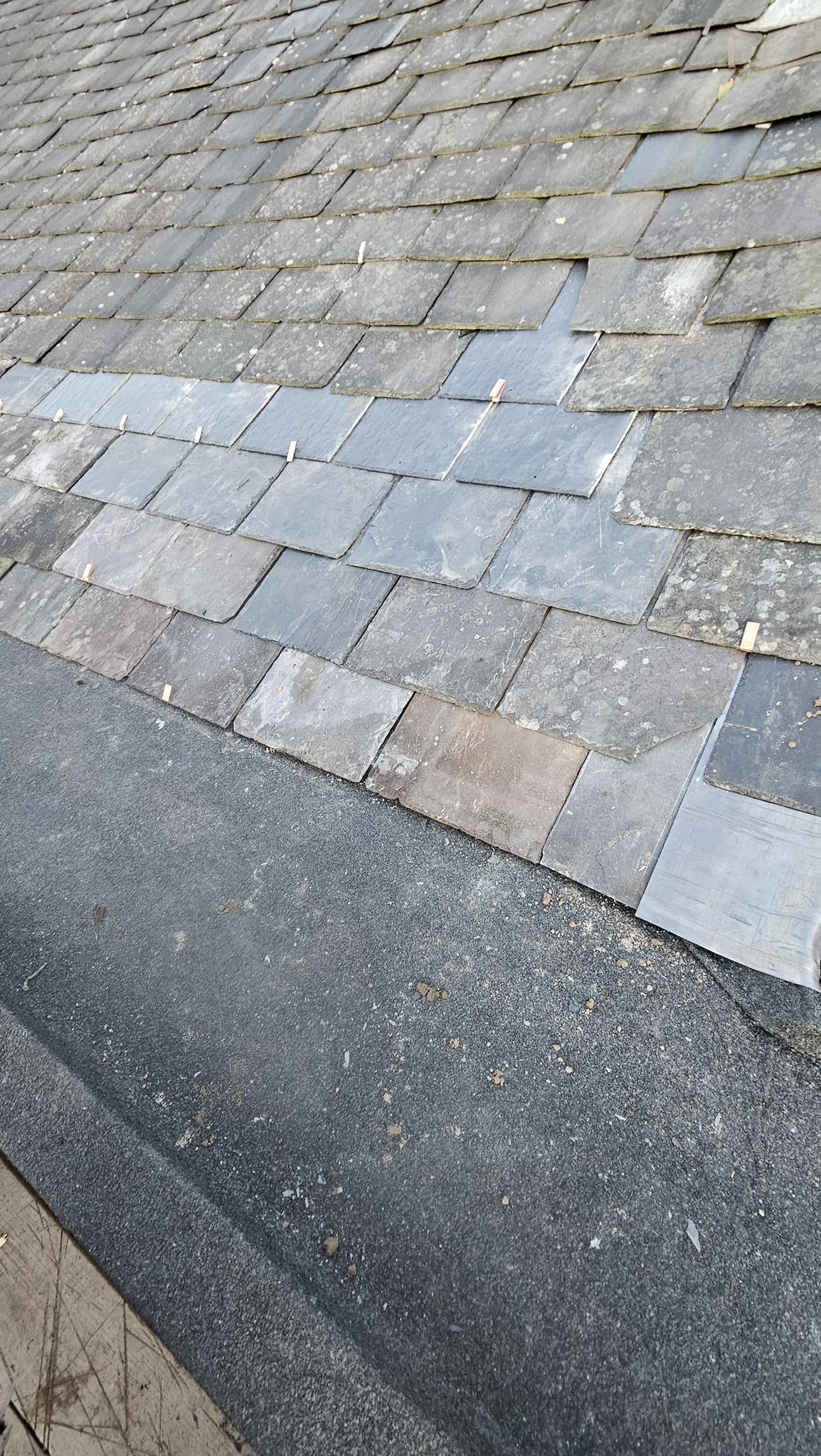 Close-up of a weathered asphalt shingle roof. Patches of lighter-colored shingles are visible.