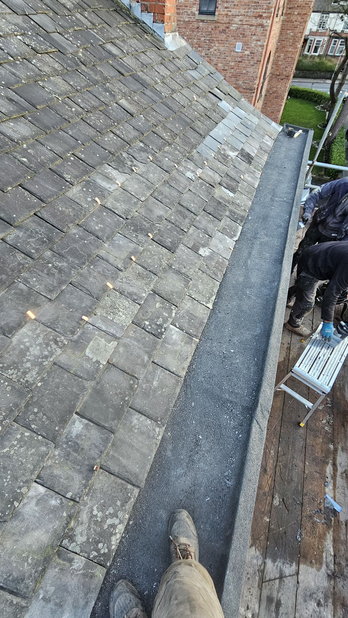Rooftop with gray slate tiles and a built-in gutter; person on a scaffold near the edge.
