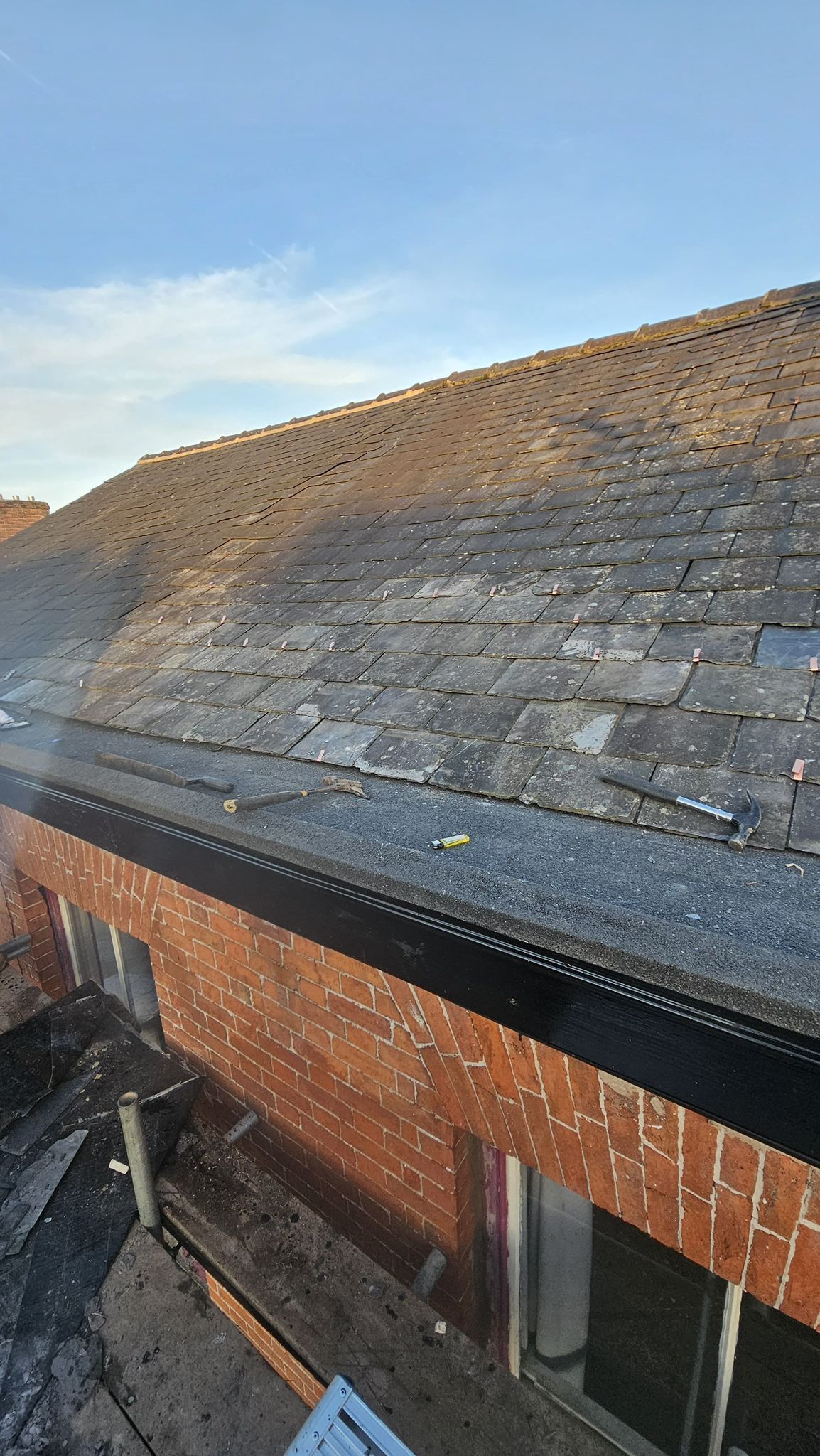Roof with slate tiles, brick wall, gutter, and a clear blue sky.