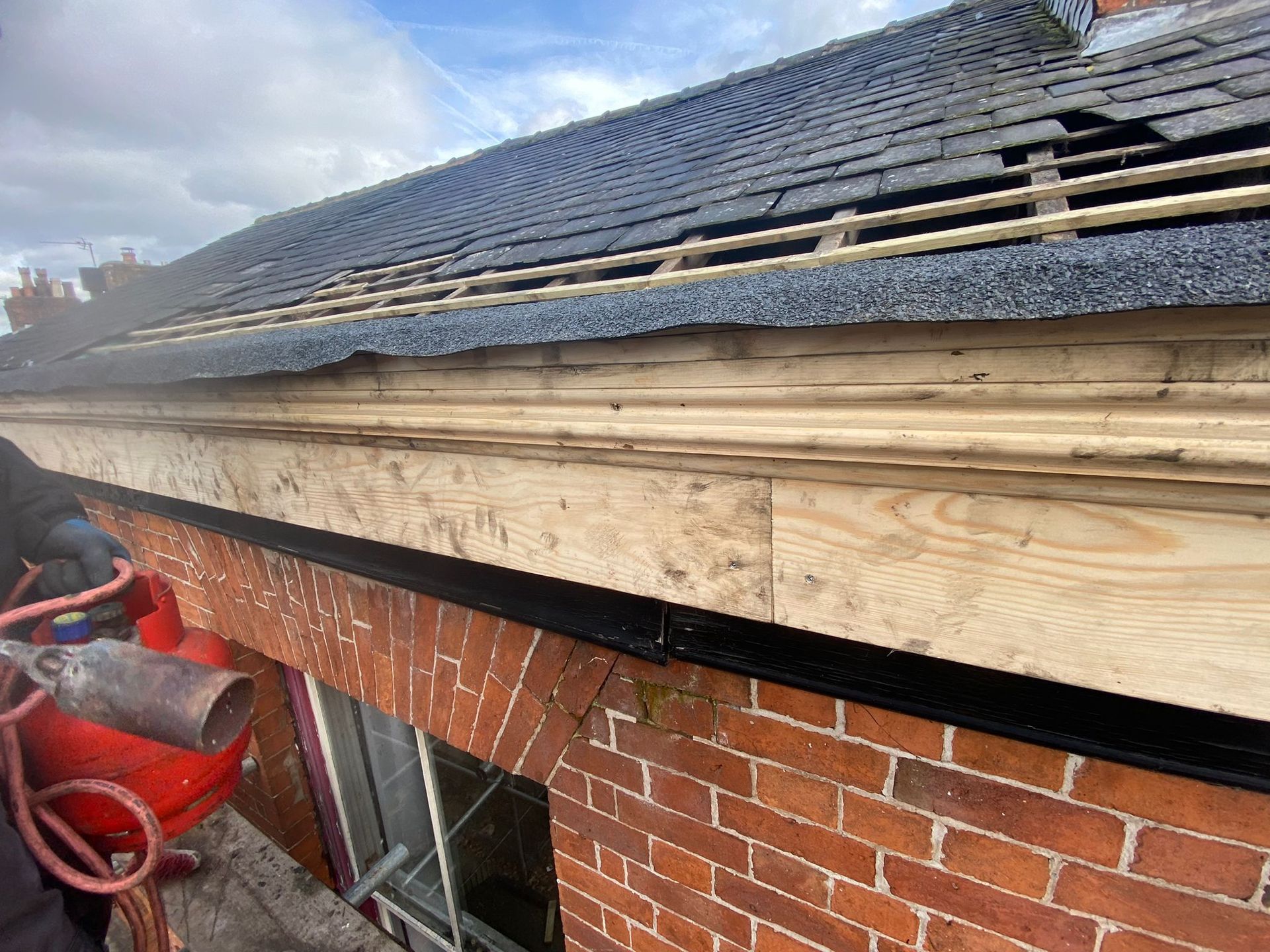 Roof being repaired, brick building, wooden trim, black roof tiles, torch in use.