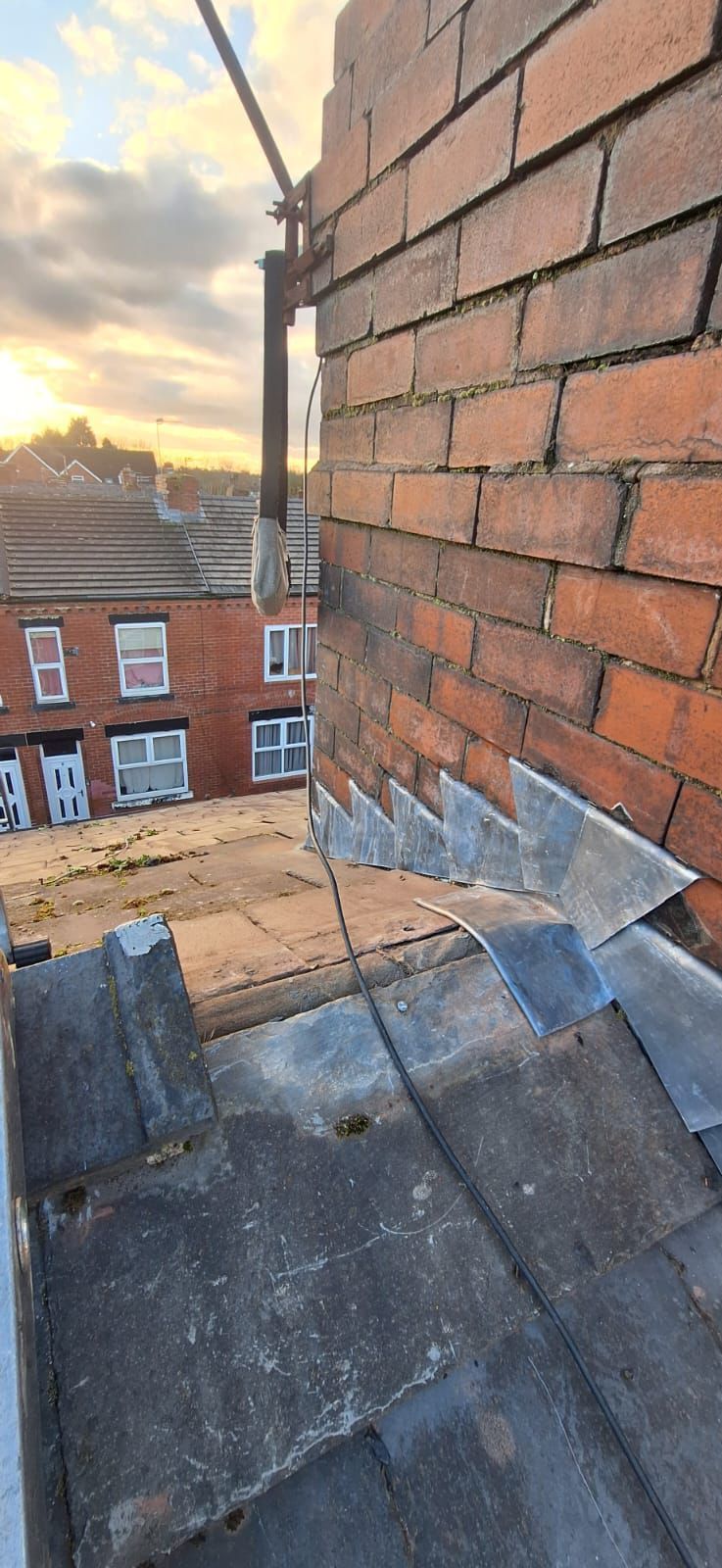 Roofing detail: brick chimney, metal flashing, and gray tiles.