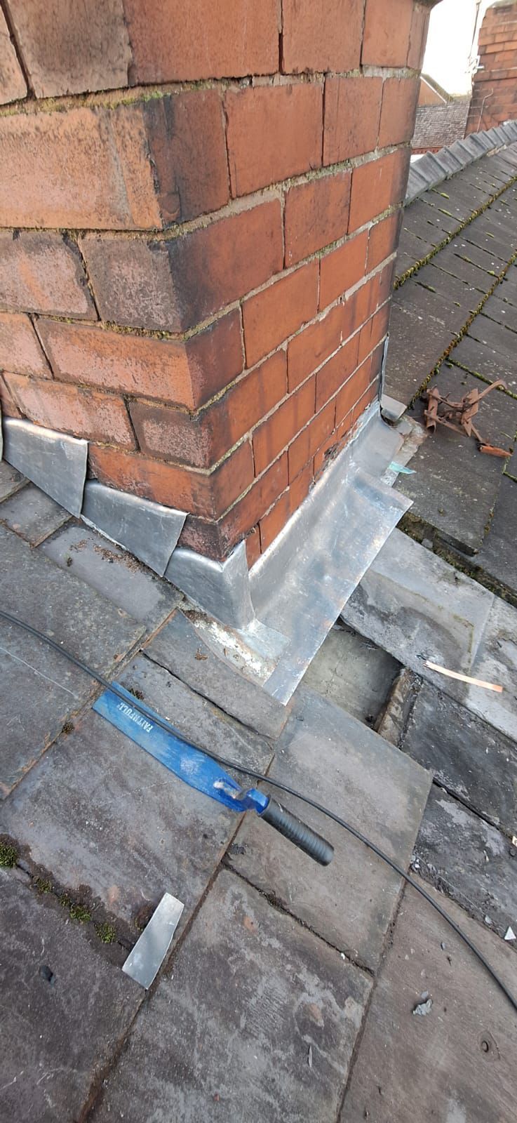 Close-up of a brick chimney on a roof with lead flashing installed around its base.