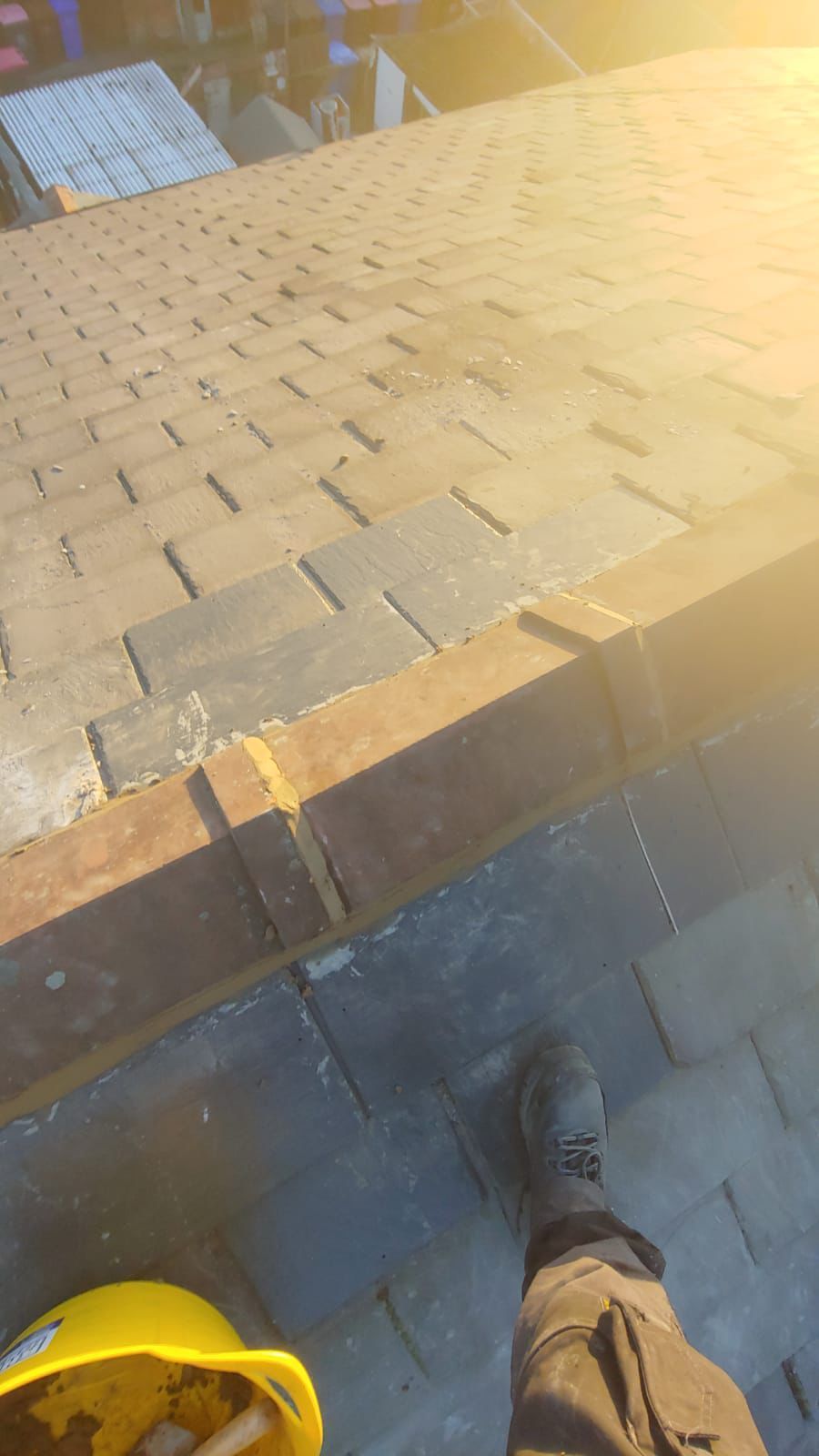 View from a rooftop: person's foot, hard hat, and roof tiles in sunlight.