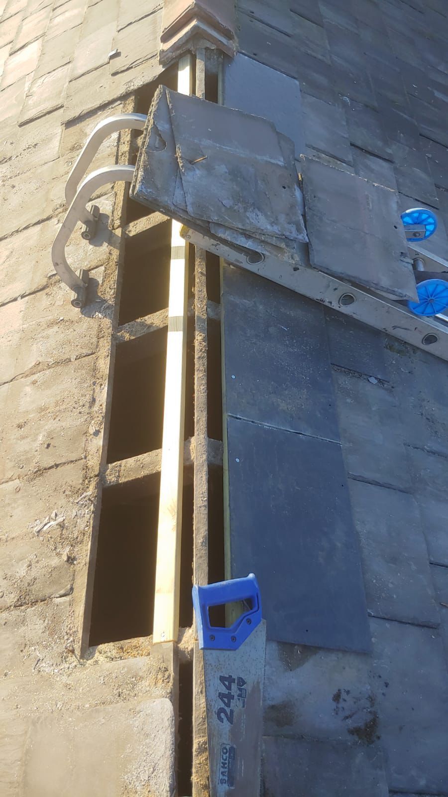 Roof repair, section of slate roof removed, revealing wooden frame, ladder hook attached.