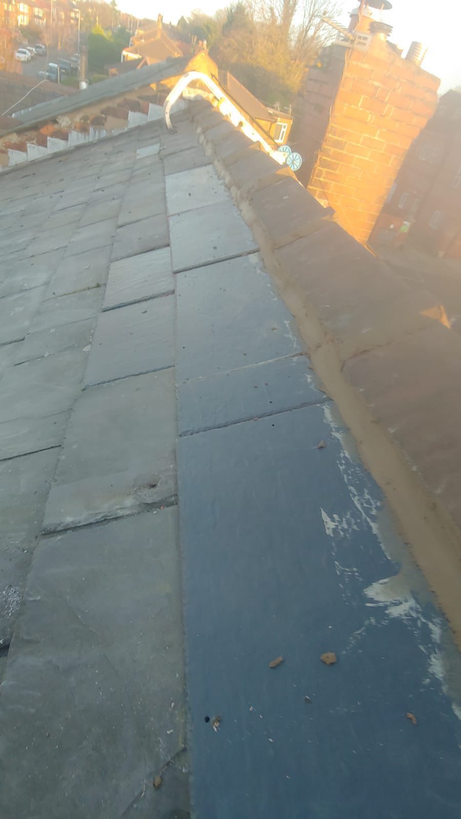 Dark slate roof with a dark gray flat section next to a brick chimney and gutter.