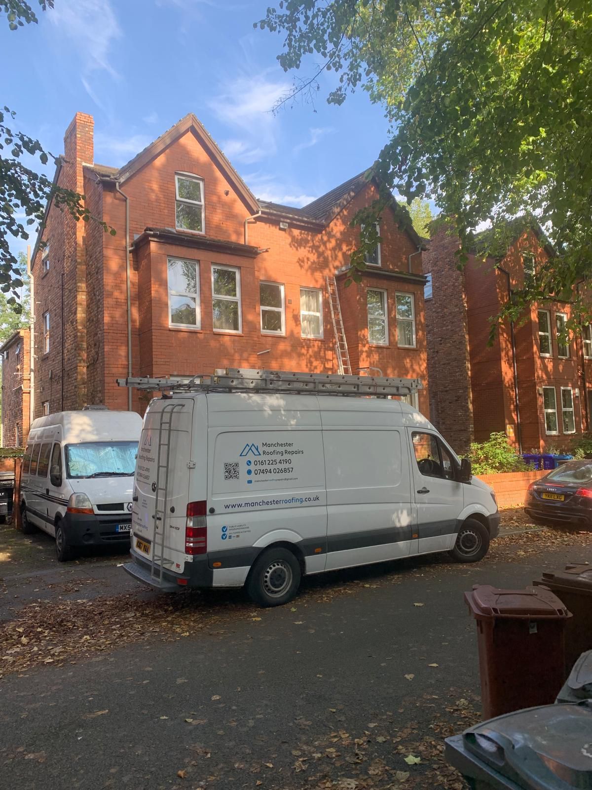 A white van is parked in front of a large brick building.