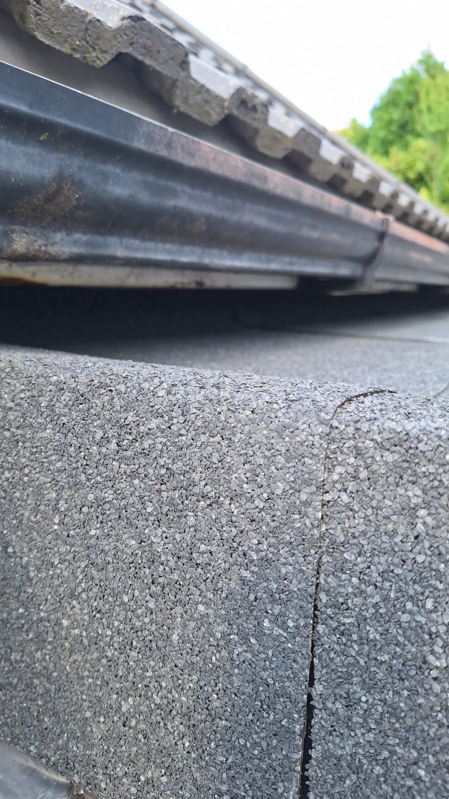 A close up of a gutter on a roof next to a brick wall.
