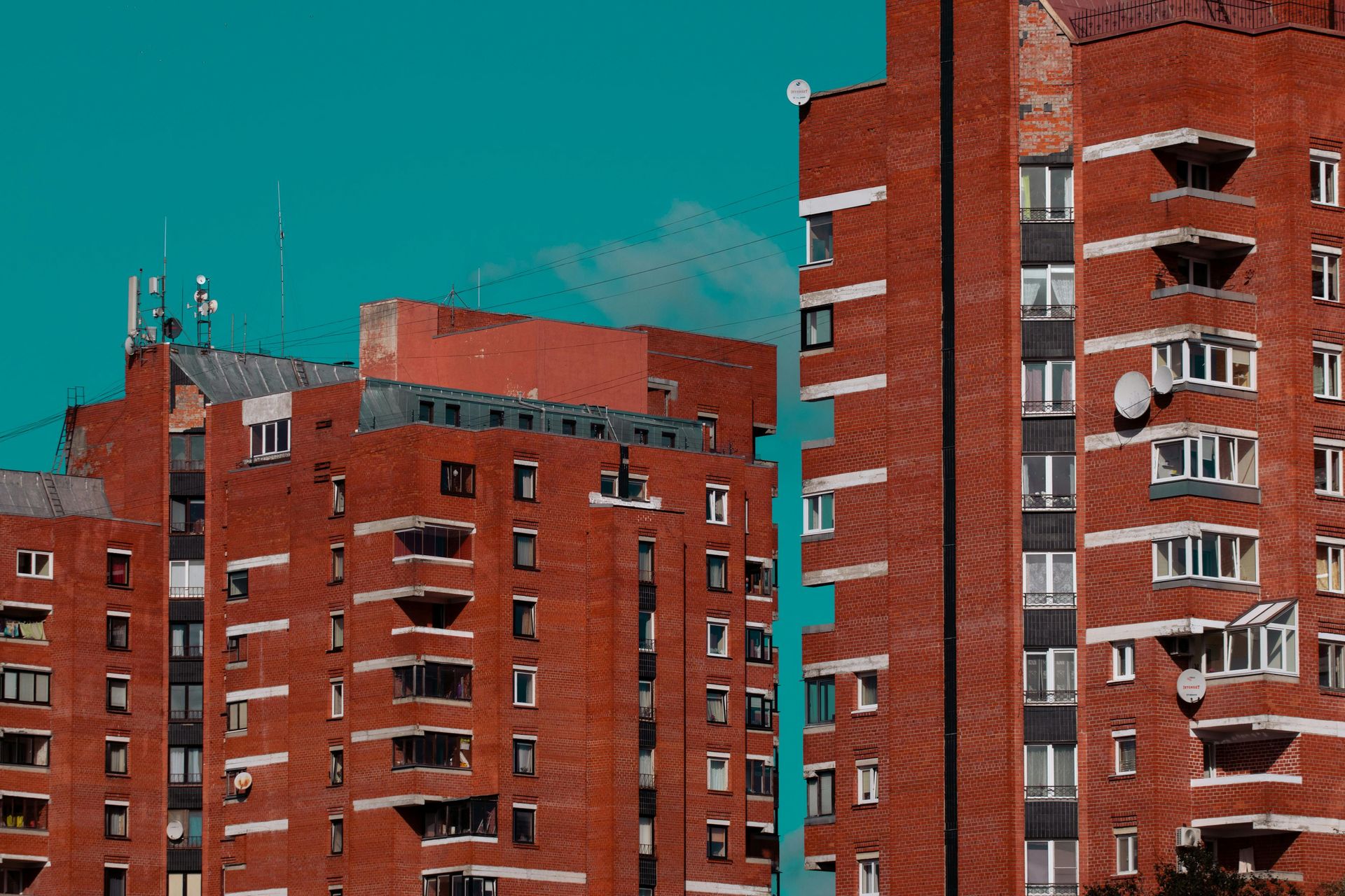 Red brick apartment buildings with many windows against a teal sky.