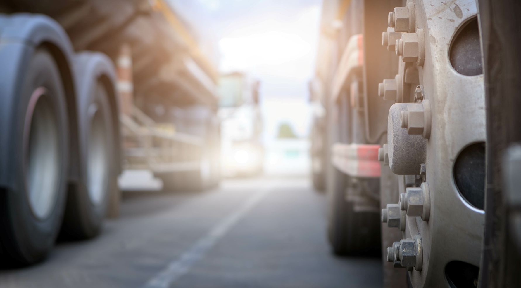 Close-up of truck wheels, others in the background, parked on an asphalt road; sun glare.