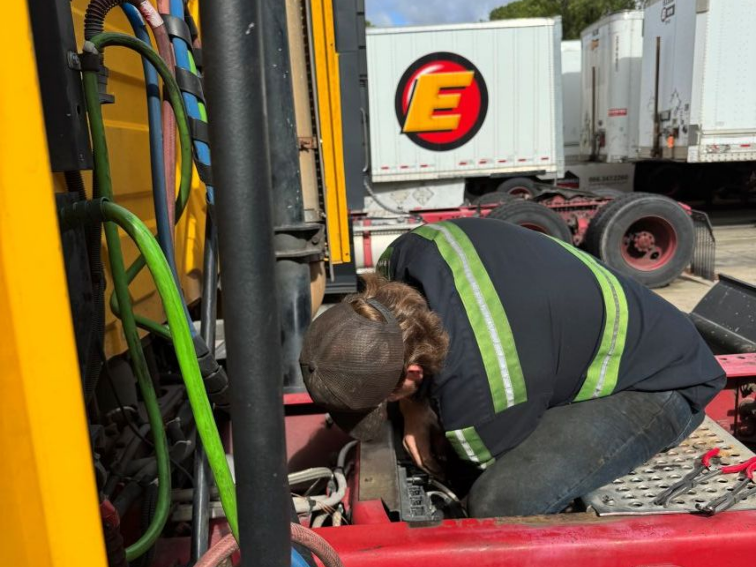 Red semi-truck driving on a road, with a white trailer, desert landscape backdrop, under a blue sky.