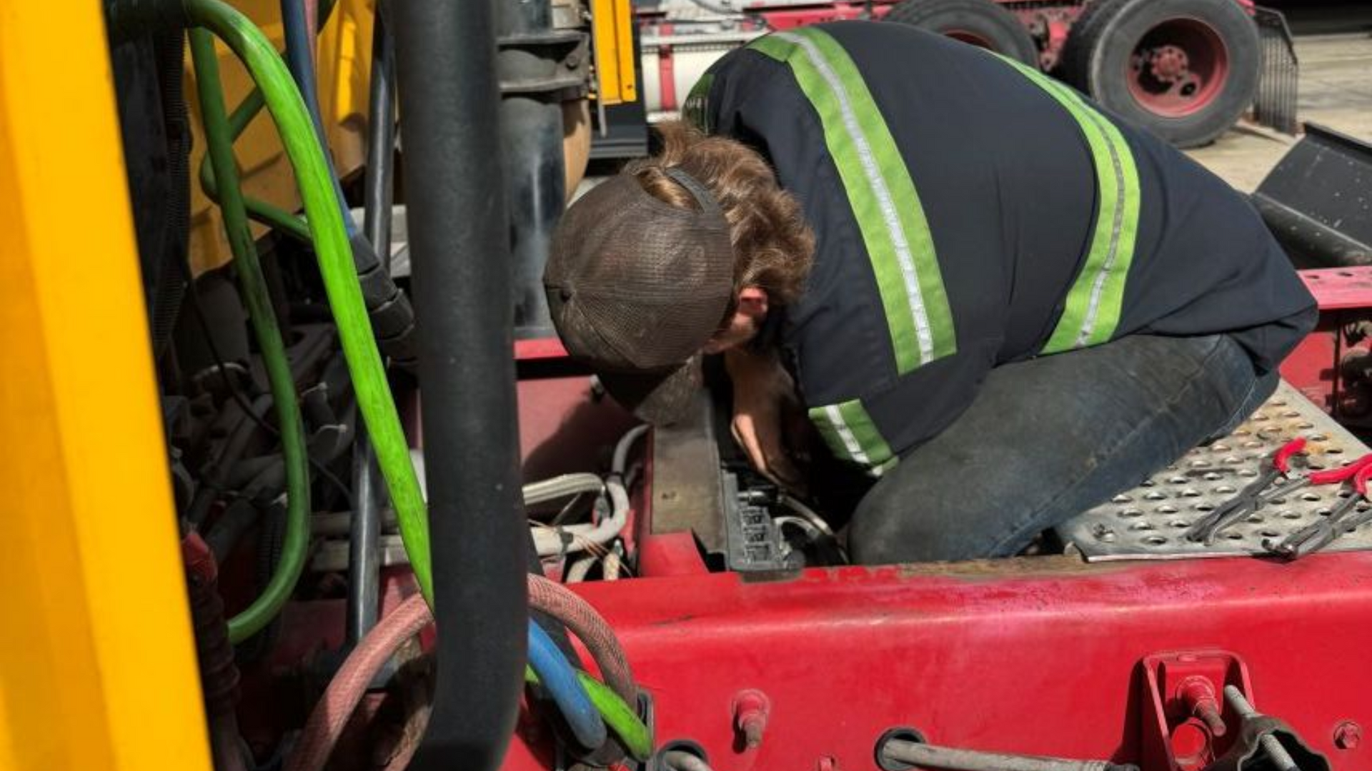 Mechanic working on the engine of a yellow and red truck, wearing a safety vest in Greensboro, NC.