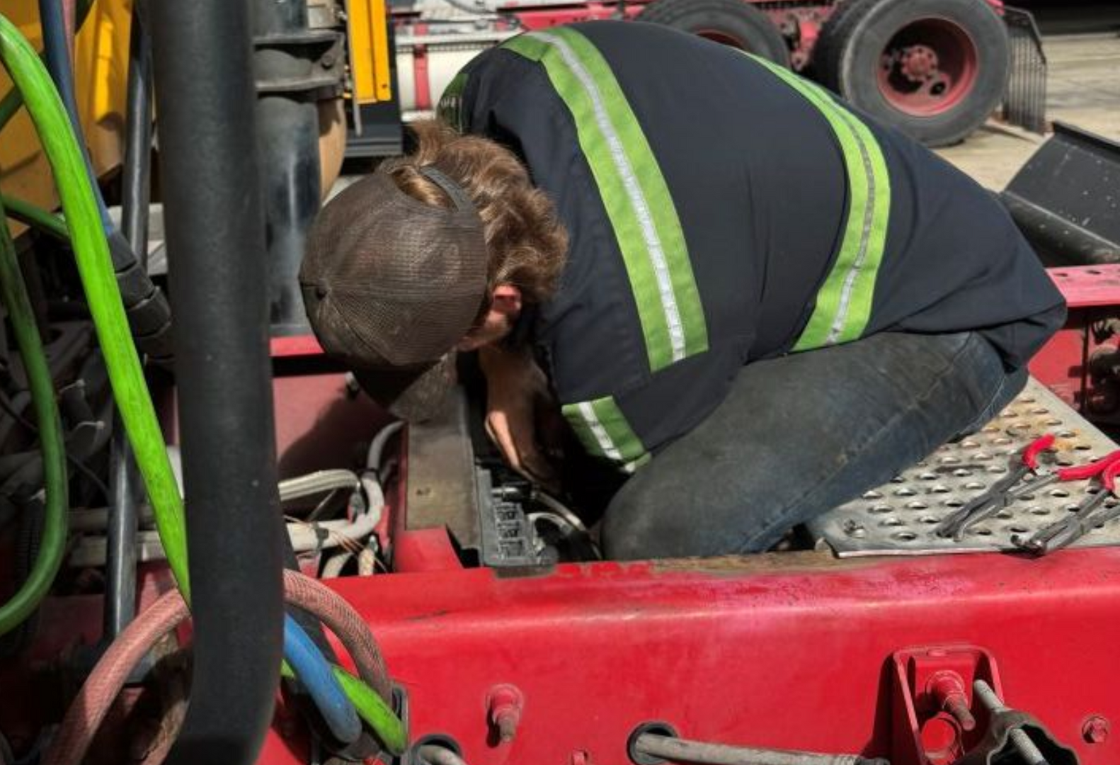 Mechanic working on the engine of a yellow and red truck, wearing a safety vest in Cary, NC.