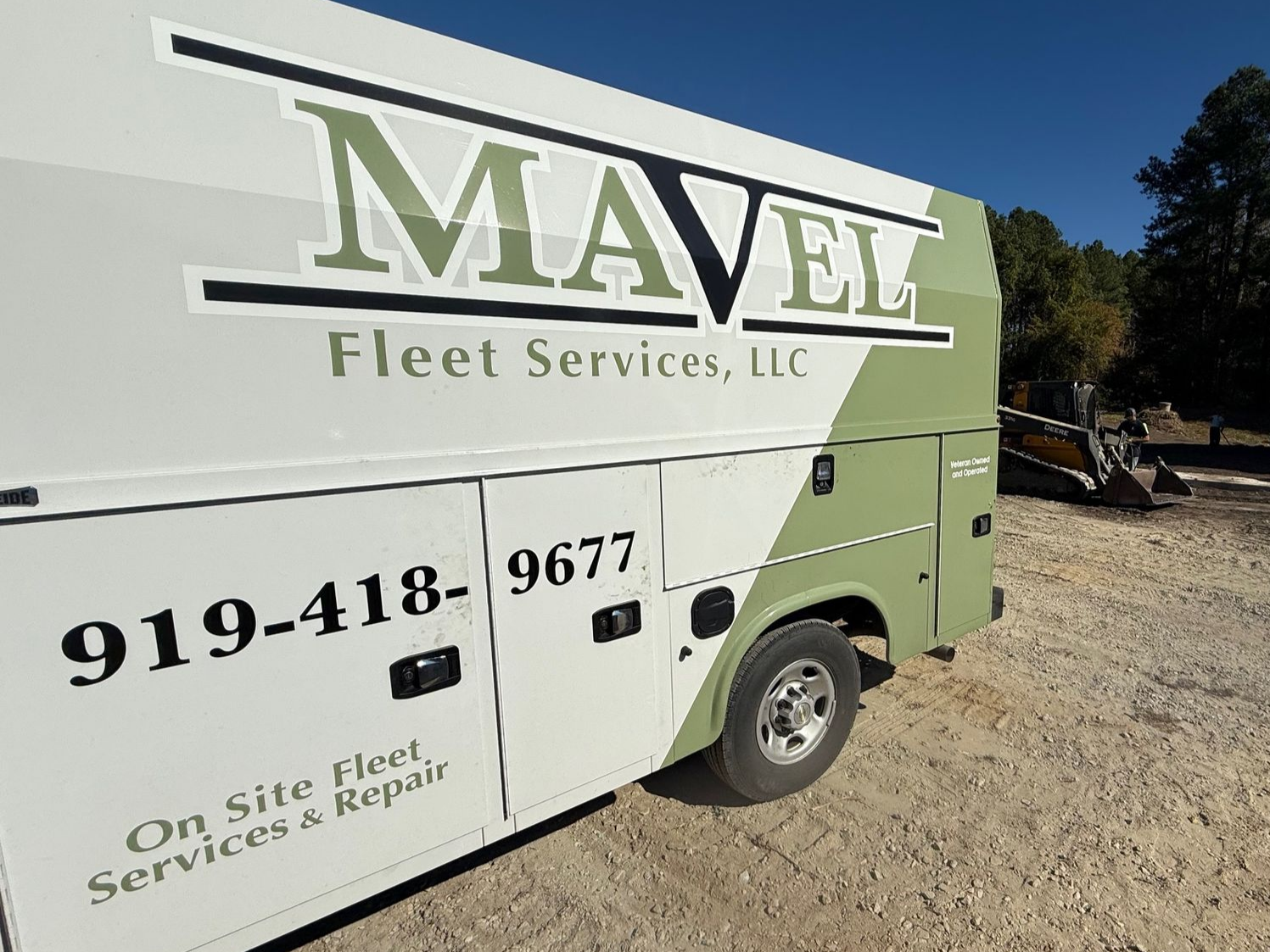 White and green Mavel Fleet Services truck on gravel, blue sky background.