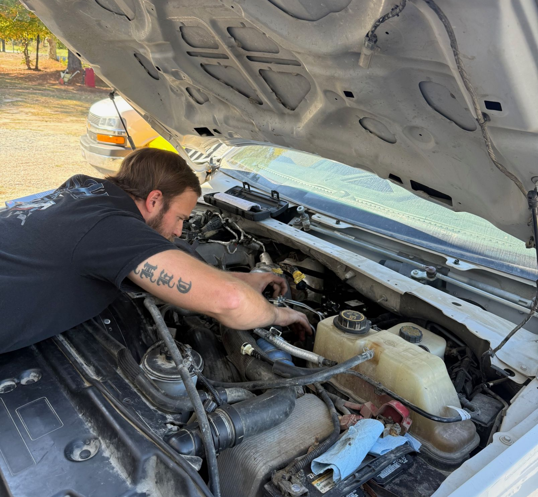 Man working on engine under the open hood of a white truck.