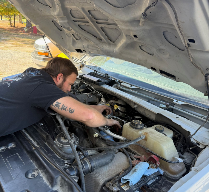 Man working on engine under the open hood of a white truck.