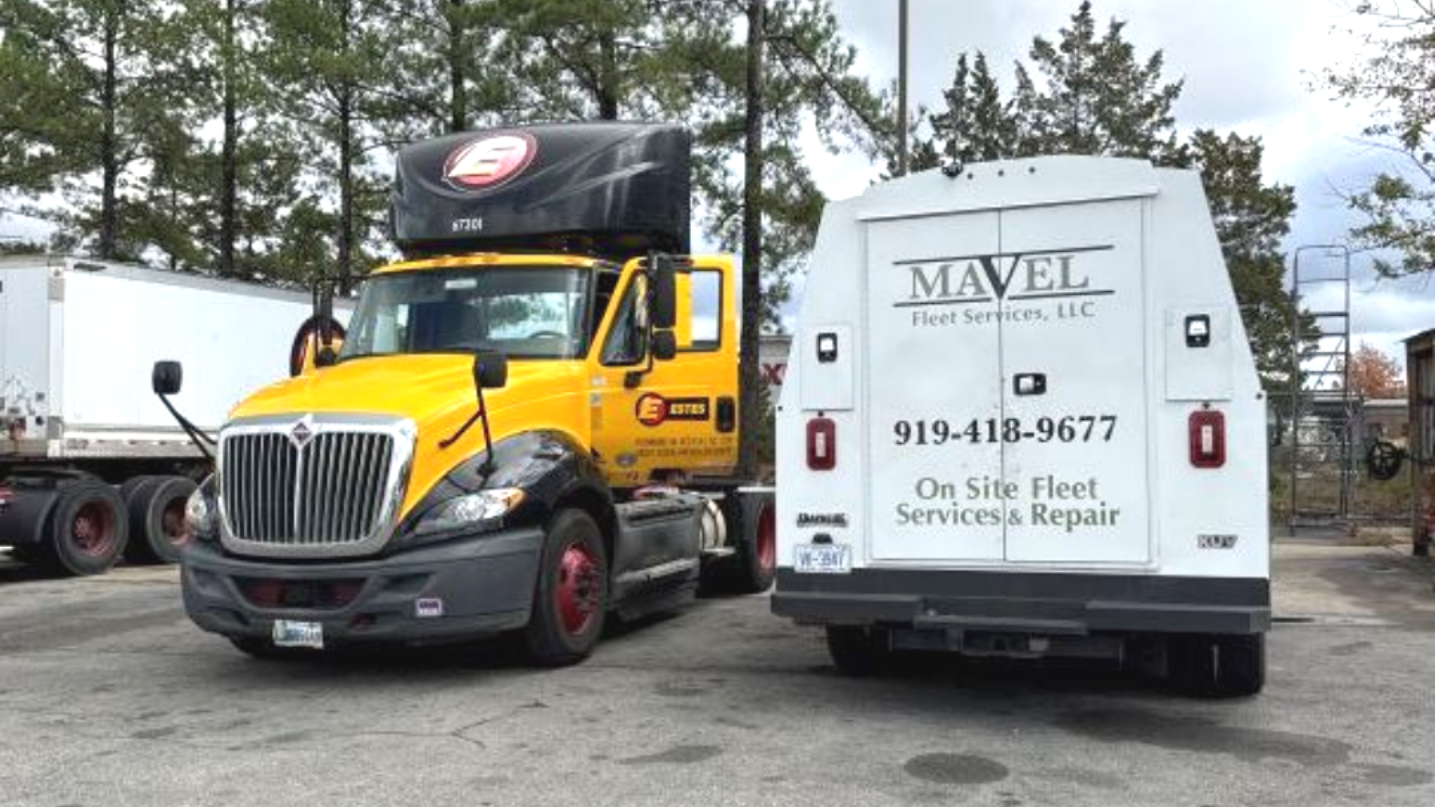Yellow semi truck next to white service vehicle; both have company logos, parked outdoors.