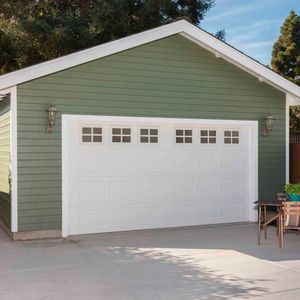 Garage vert avec boiseries et porte de garage blanches ; une table et des chaises sont placées devant.