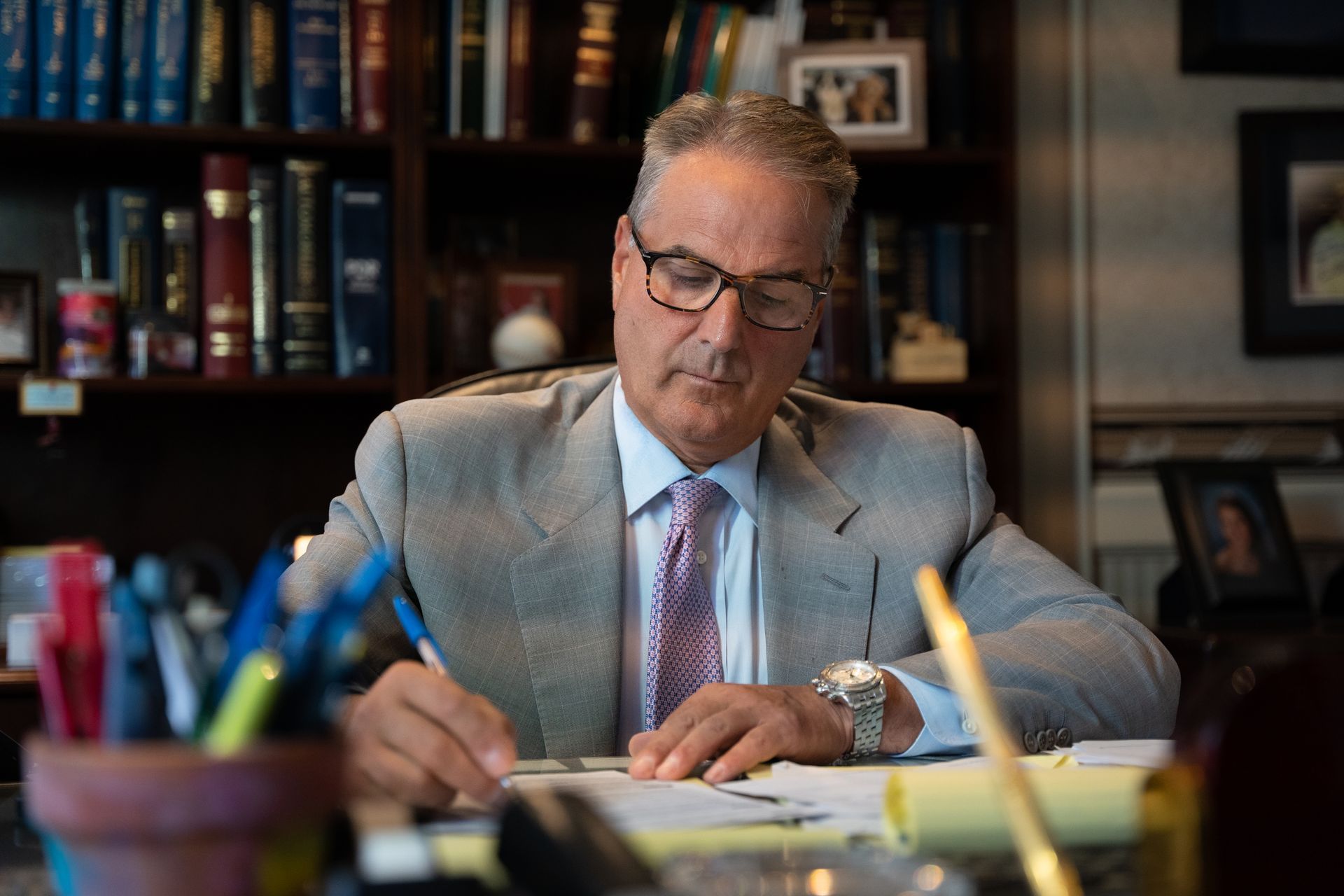 A man in a suit and tie is sitting at a desk writing on a piece of paper.