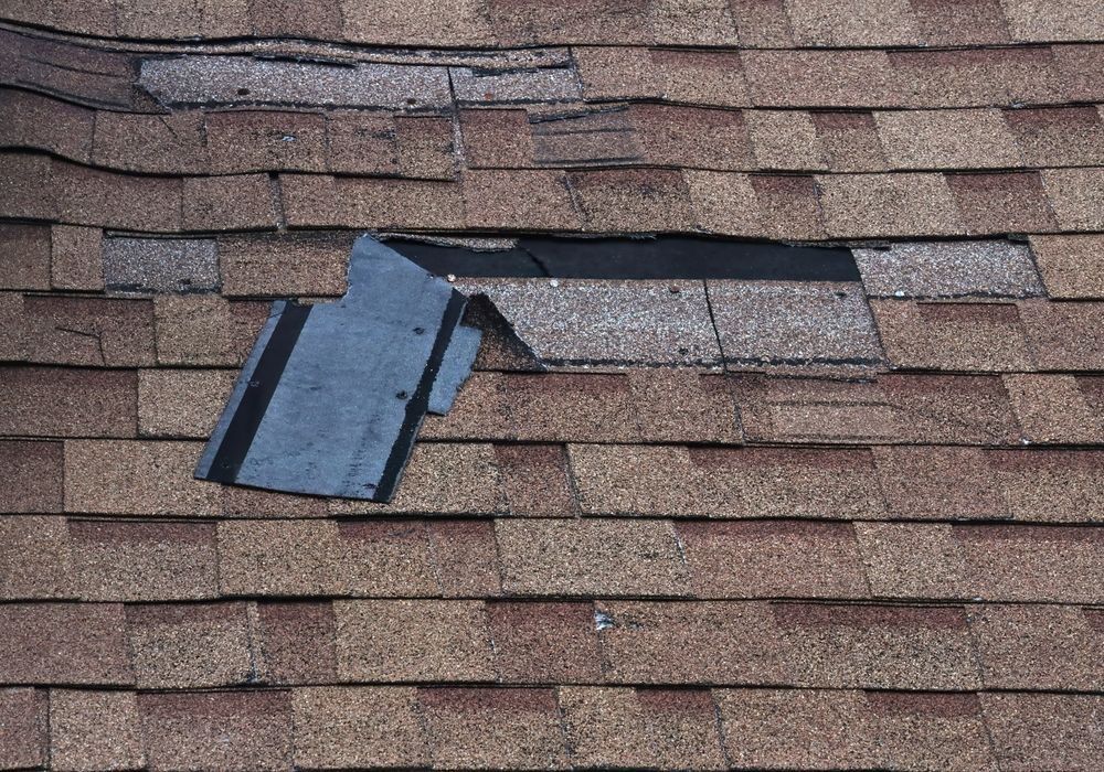 Damaged asphalt shingle roof with a large hole and missing shingles, exposing underlayment.