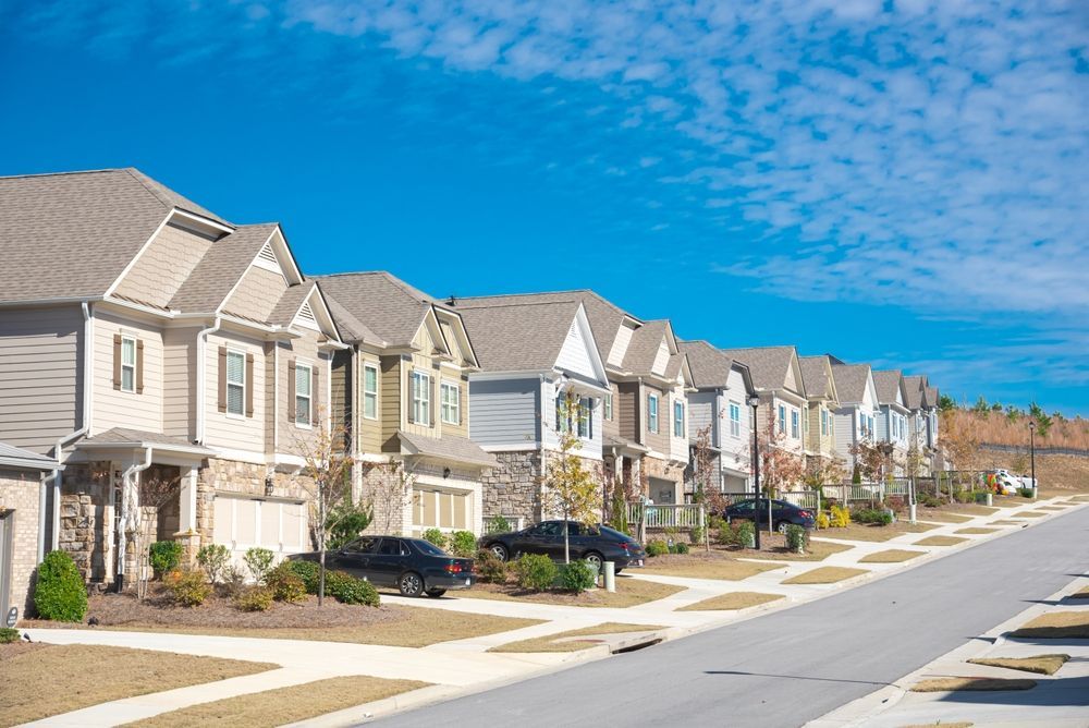 Row of suburban homes on a sunny day. Blue sky, brown roofs, cars parked along the street.