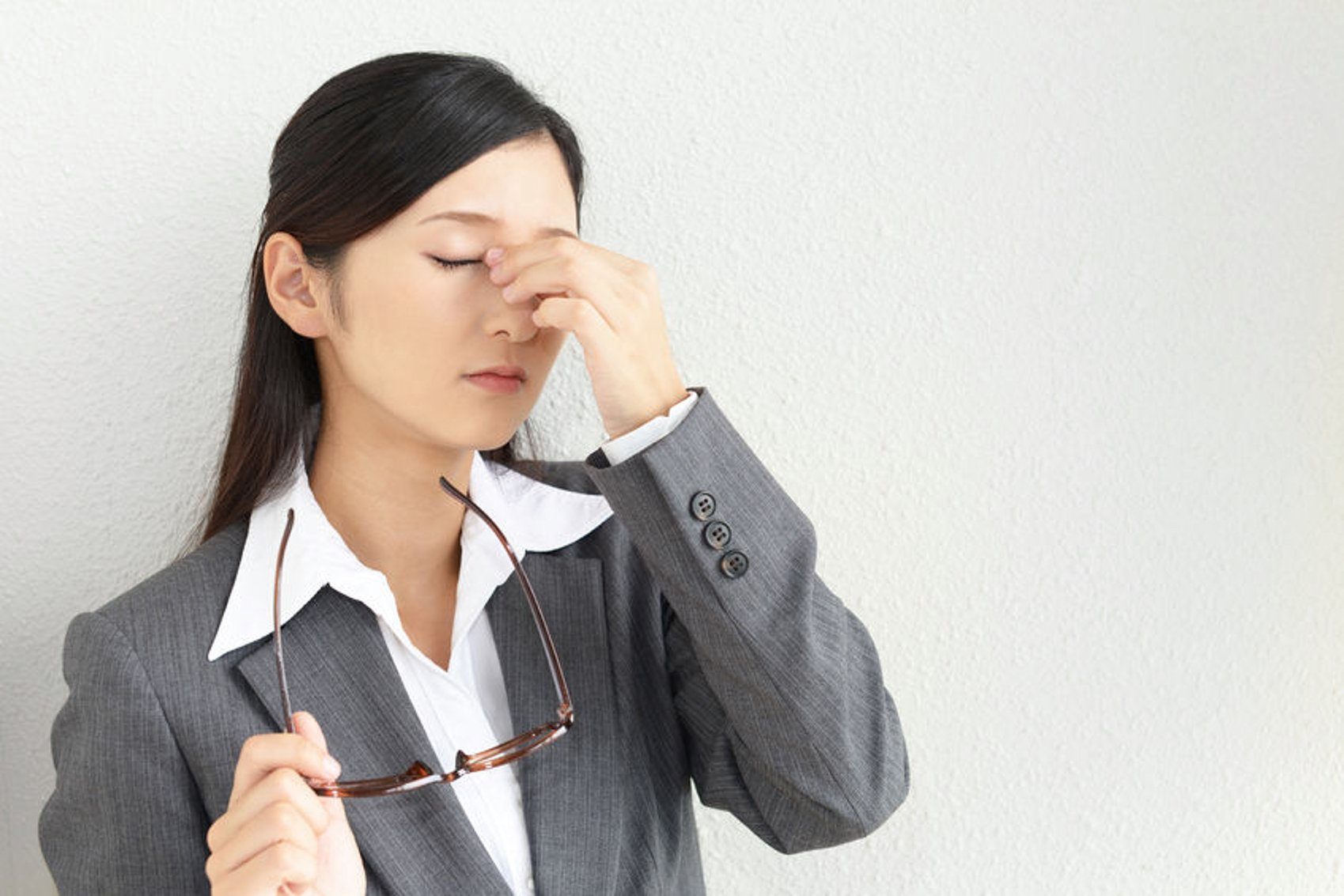 A woman in a suit is holding her glasses and rubbing her eyes.