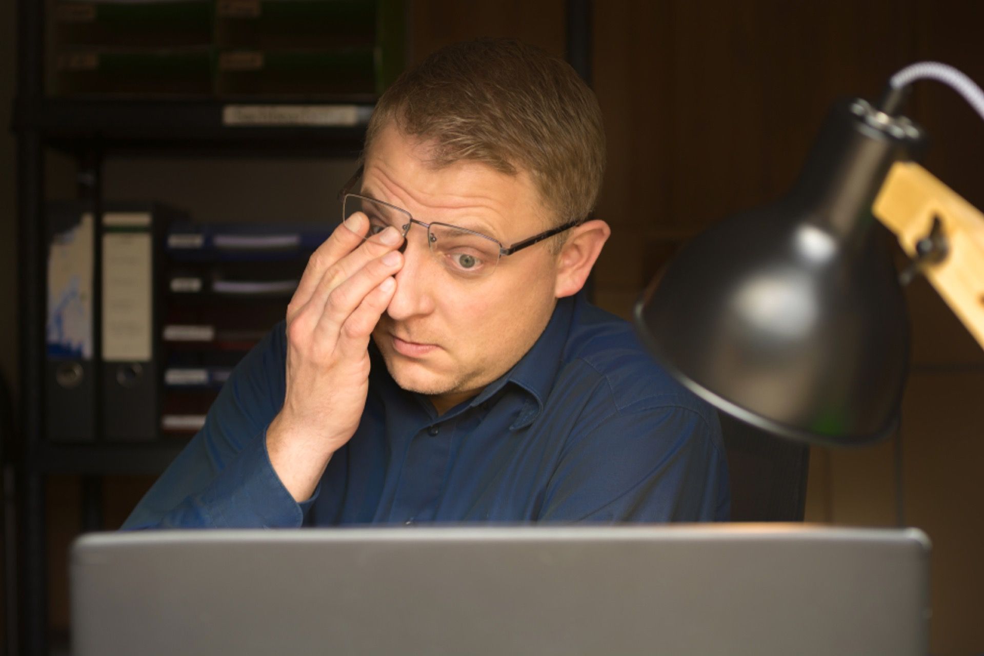 A man is rubbing his eyes while sitting in front of a laptop computer.