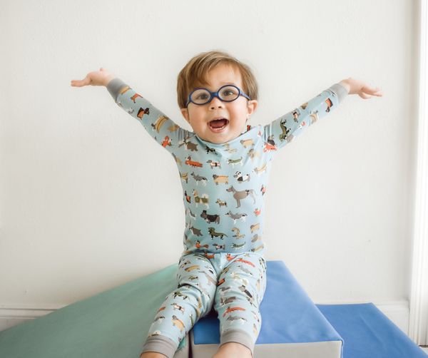 A young boy wearing glasses is sitting on a block with his arms outstretched.