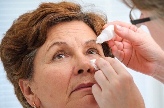 A woman is getting eye drops from a doctor.