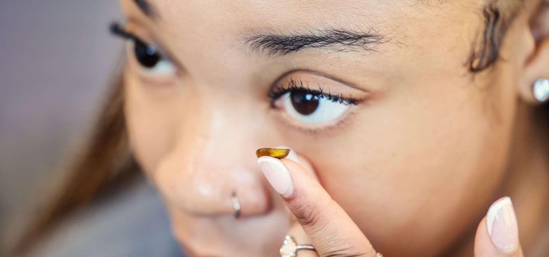 Person holding a brown contact lens, preparing to insert it into their eye.
