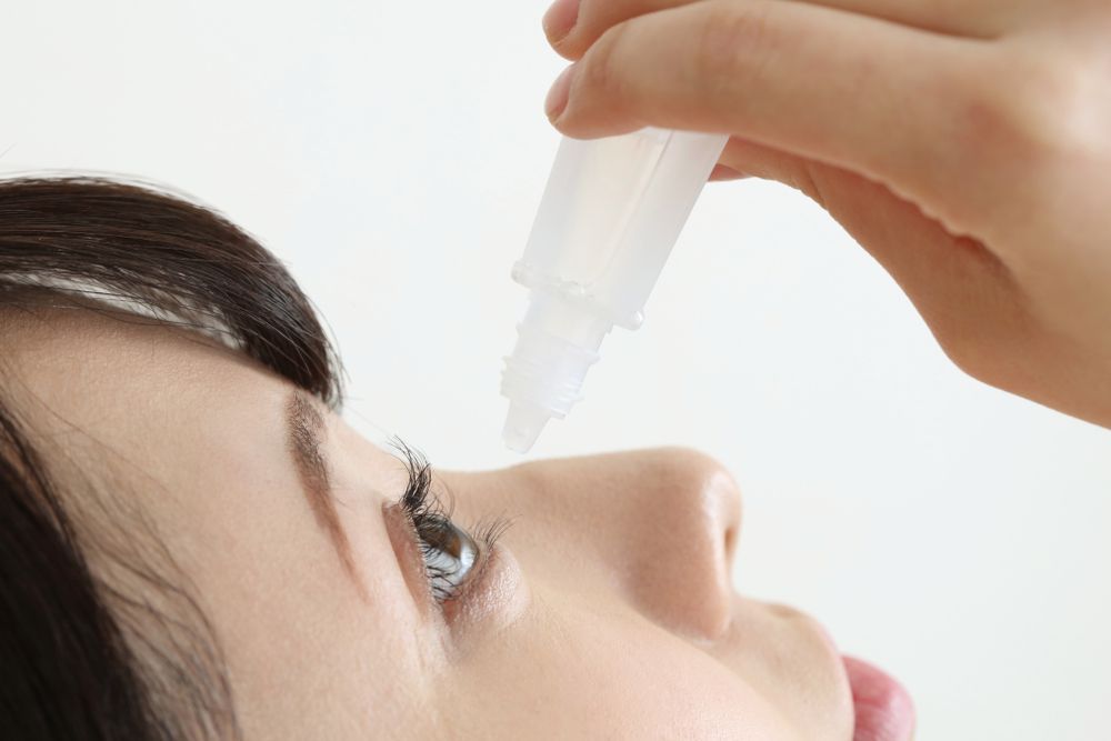 A woman is applying eye drops to her eye.