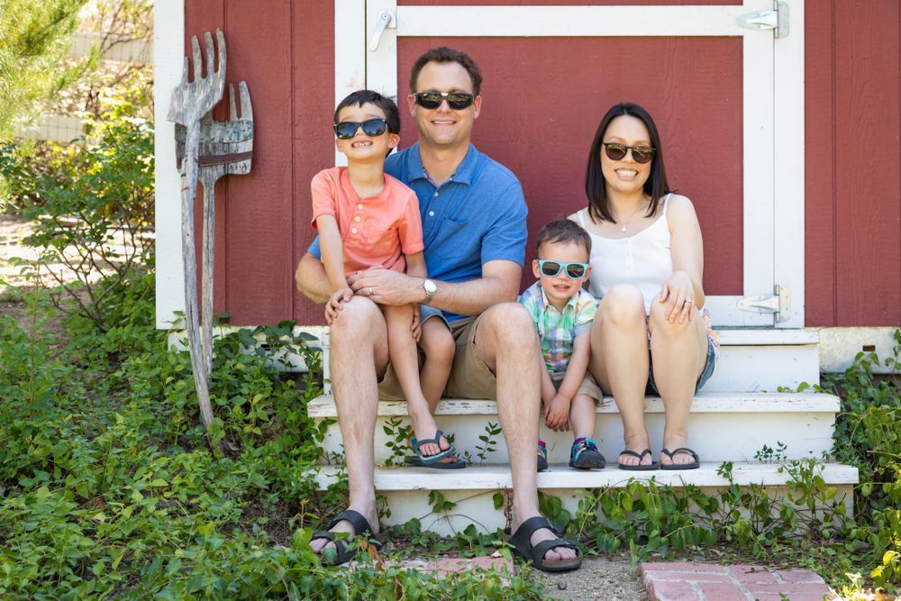 A family is sitting on the steps of a red shed wearing sunglasses
