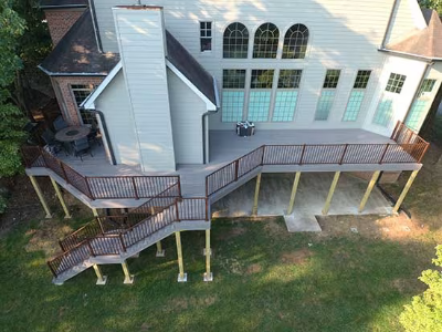 Elevated wooden deck with stairs and railings. Beige house in the background. Green lawn.