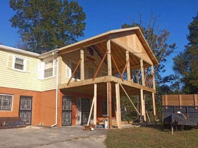 Two-story house with new wooden deck construction. Yellow siding and orange stucco. Trees in background.