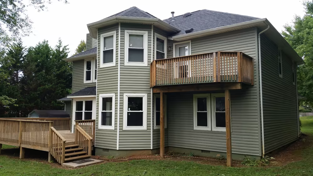 Two-story house with green siding, wooden decks, and a dark roof.