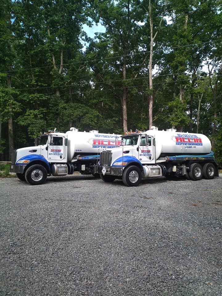 Two white tanker trucks parked on gravel in front of trees