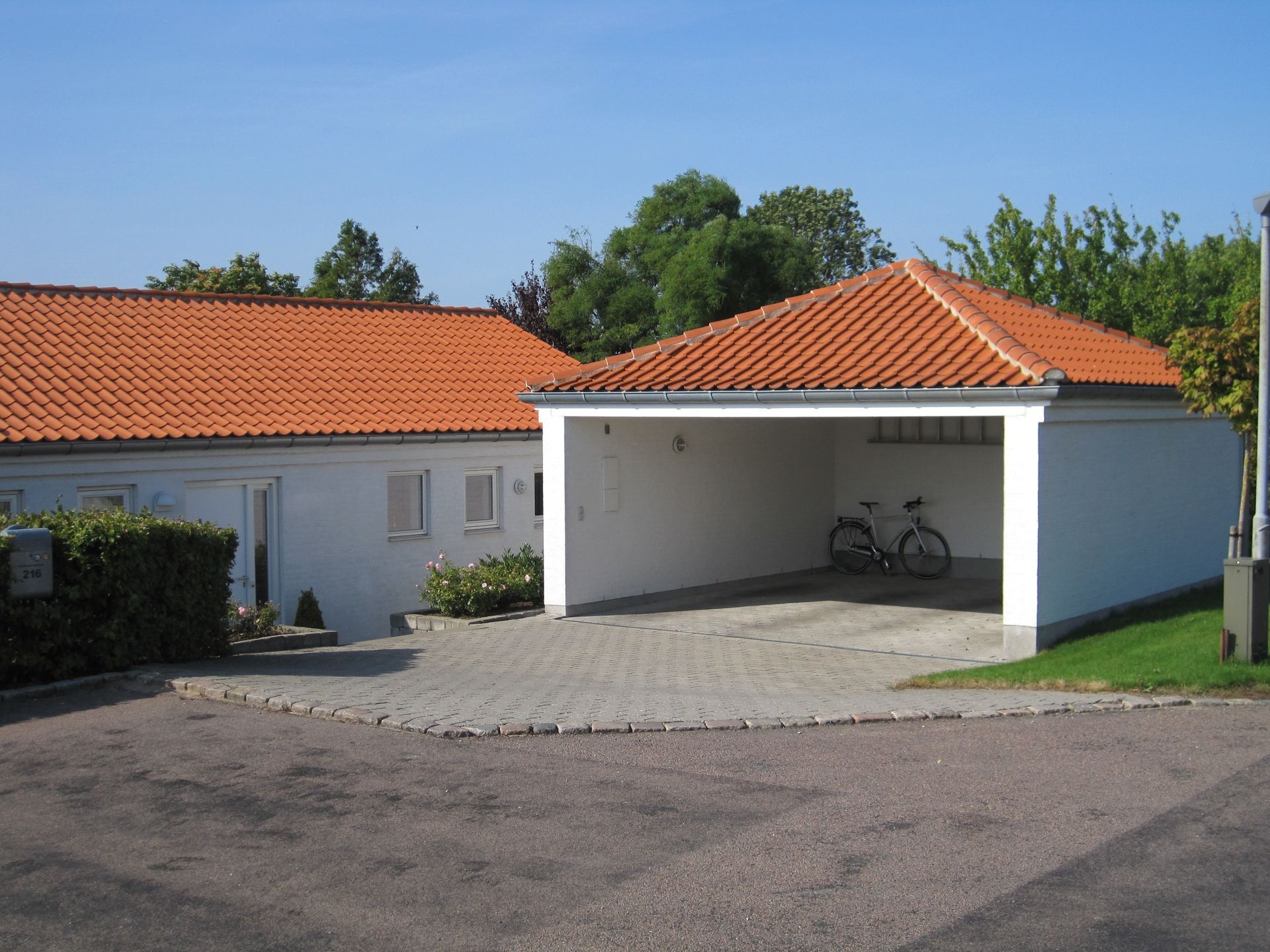 Hvidt hus og carport med orange tegltage. Cykel parkeret i carporten.