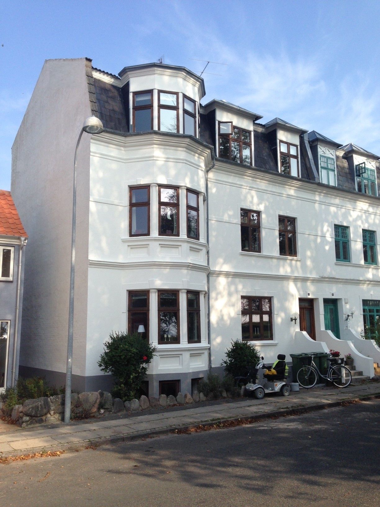 Hvid bygning i flere etager med karnap og mørkt tag.