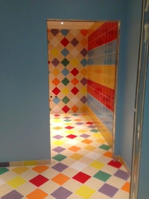 En døråbning med farverigt diamantmønstret flisegulv og -vægge. Blå væg til venstre.