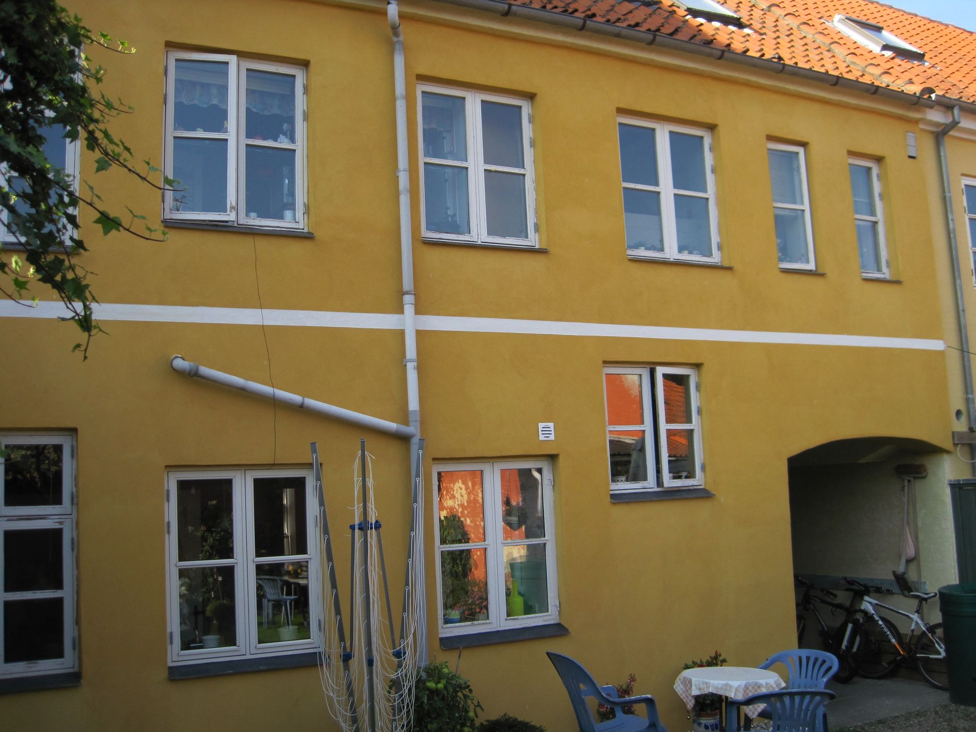 Gul bygning med hvidindrammede vinduer, en lys vandret stribe og en lille buegang.